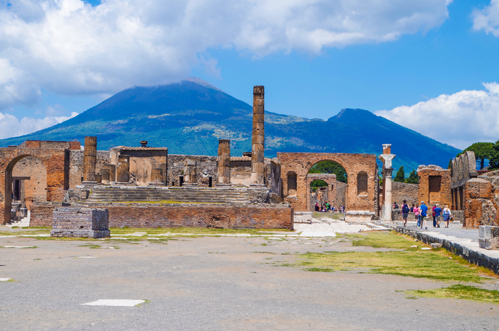 Pompeii, Archeological Site: Ancient Ruins Of The Temple Of Jupiter With View On Smoking Mount Vesuvius.