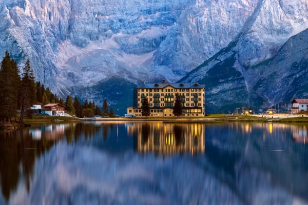 השתקפות של בית מלון באגם מיסורינה בדולומיטים האיטלקיים עם הרים מושלגים ברקע