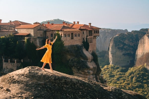אישה המטיילת במטאורה מצטלמת בחינניות על רקע הנוף הייחודי ואחד מהמנזרים האייקוניים של האזור