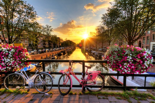 זריחה מעל תעלה בקיץ באמסטרדם, גשר עם אופניים ופרחים